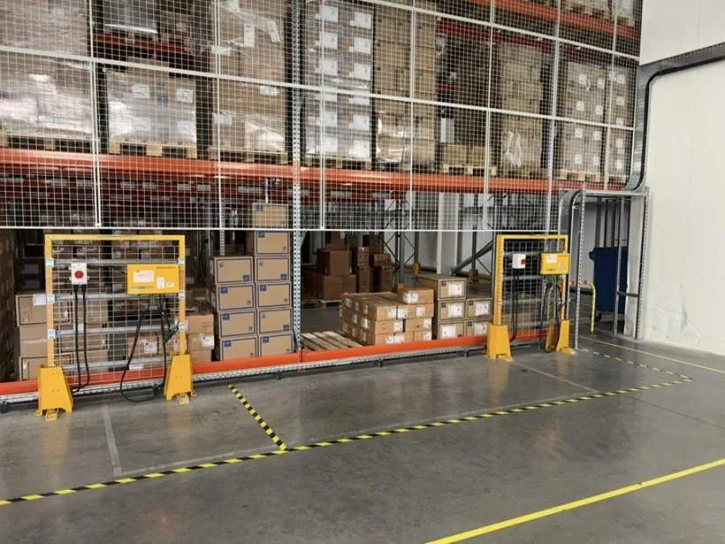 Two forklift battery chargers with rotary isolators mounted in protective frames at the foot of warehouse racking, Bicester