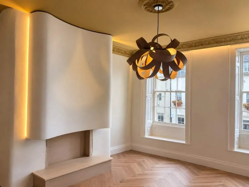 Warm LED strip lighting outlining a sculpted curved chimney breast, with a ribbon wood pendant and cornice uplighting in a period room, part of a four-storey rewire in Woodstock, Oxfordshire