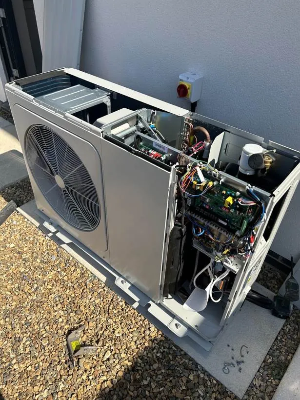 Air source heat pump outdoor unit with its service cover off during commissioning, beside a rotary isolator, Marcham near Abingdon