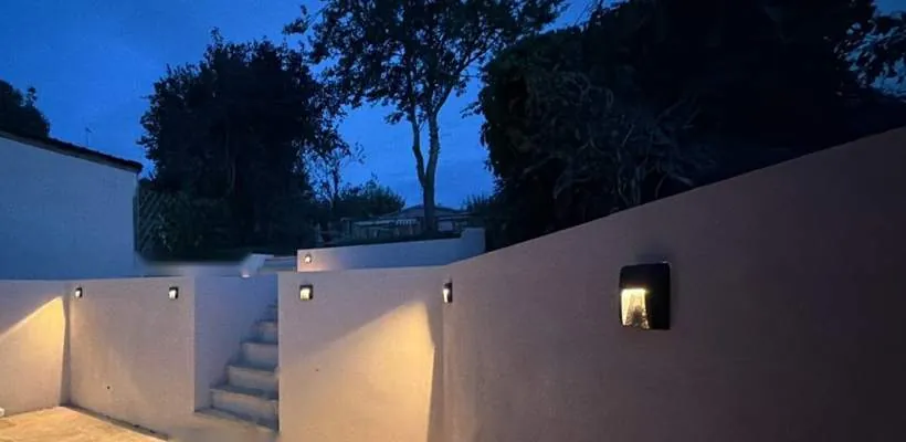 Row of recessed outdoor wall lights washing warm light down a newly rendered retaining wall and steps at dusk, Hempton, Oxfordshire