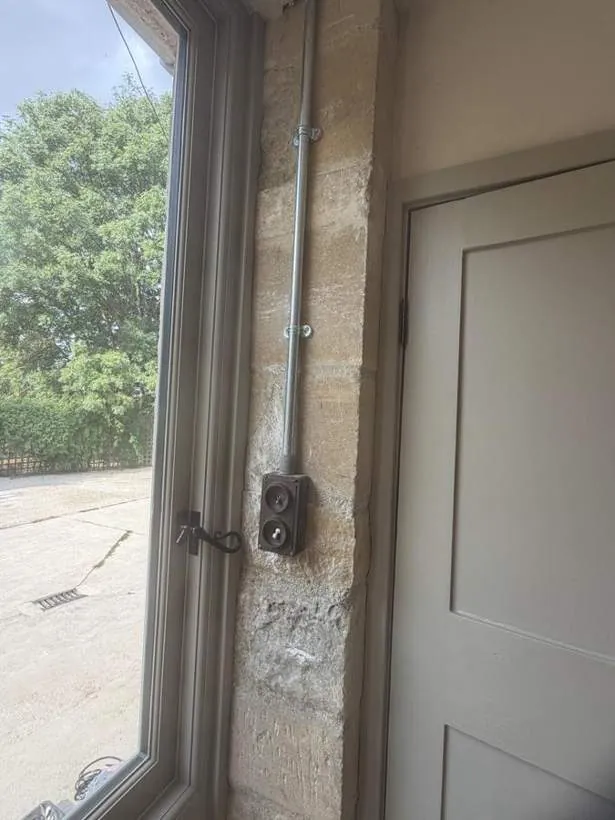Galvanised steel conduit dropping to a reclaimed switch on a stone reveal beside a garden door, Charlbury