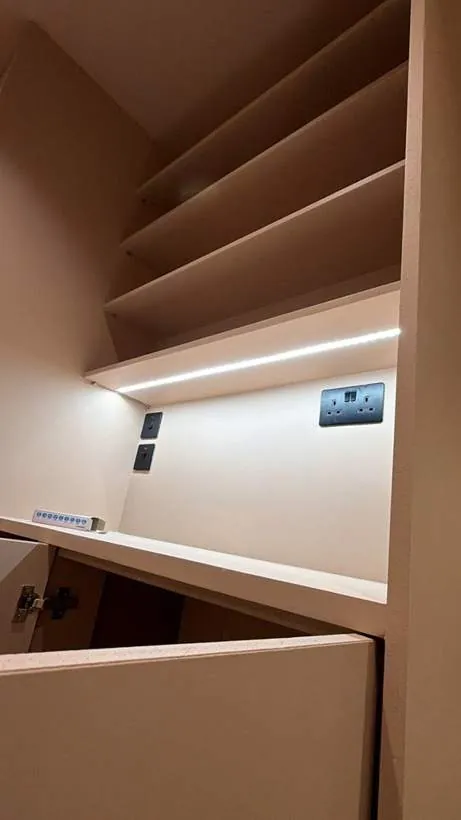 LED strip lighting under a shelf above black double sockets and switched spurs in a fitted salon unit, Lechlade