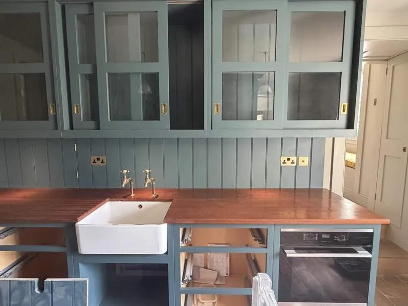 Bespoke green kitchen with antique brass sockets and under-cupboard lighting above a timber worktop and Belfast sink, Kiddington