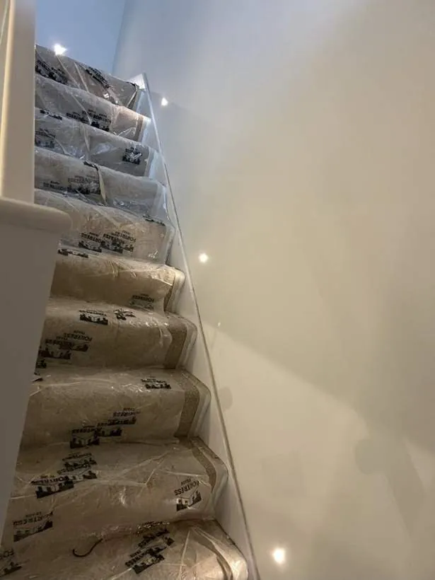 Recessed step lights set into a solid wall, glowing down a staircase with protection still over the new carpet, Adderbury