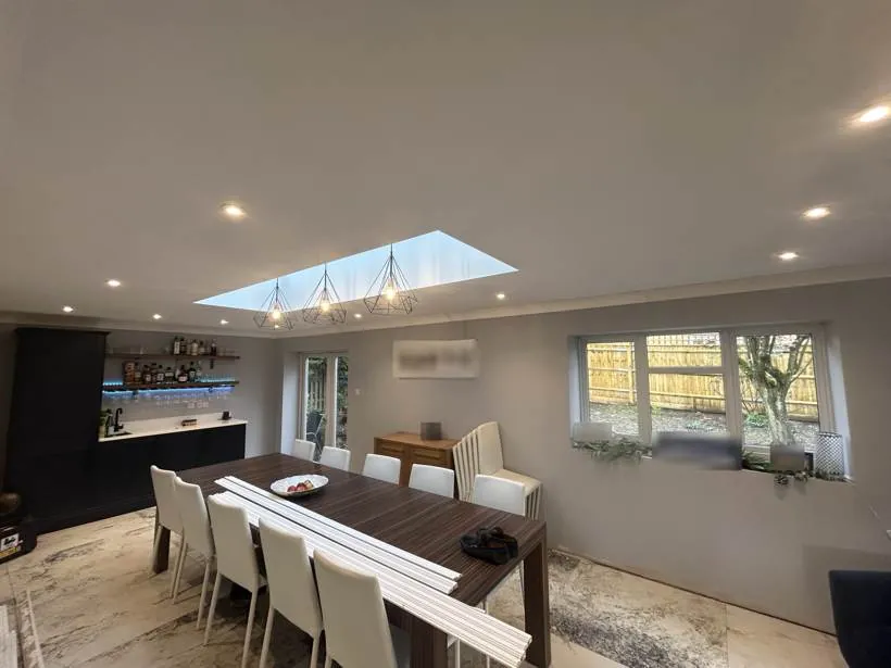 Dining extension with recessed downlights, three geometric pendants and blue LED shelf lighting above a home bar, Brackley