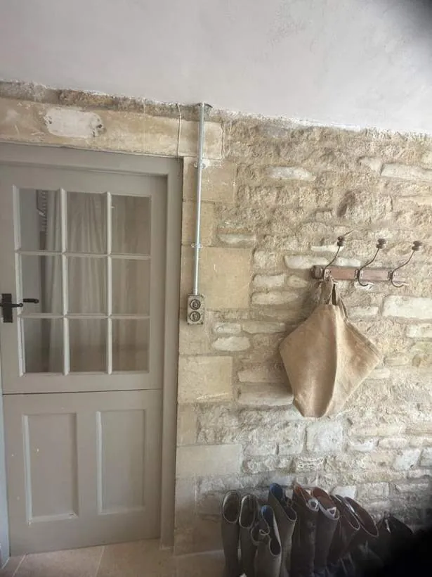 Galvanised conduit drop to a reclaimed switch on an exposed Cotswold stone wall beside a period door, Charlbury