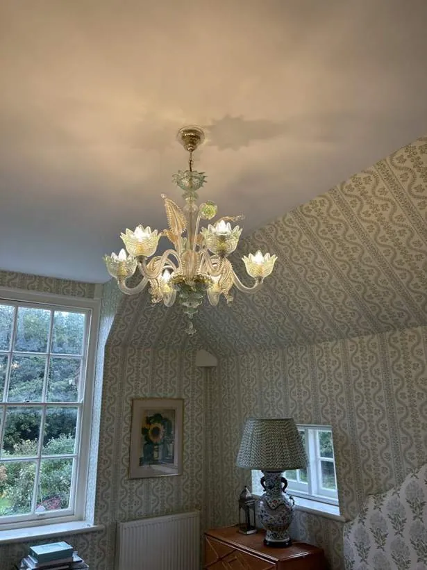 Ornate glass chandelier lit in a bedroom with patterned wallpaper and sash windows
