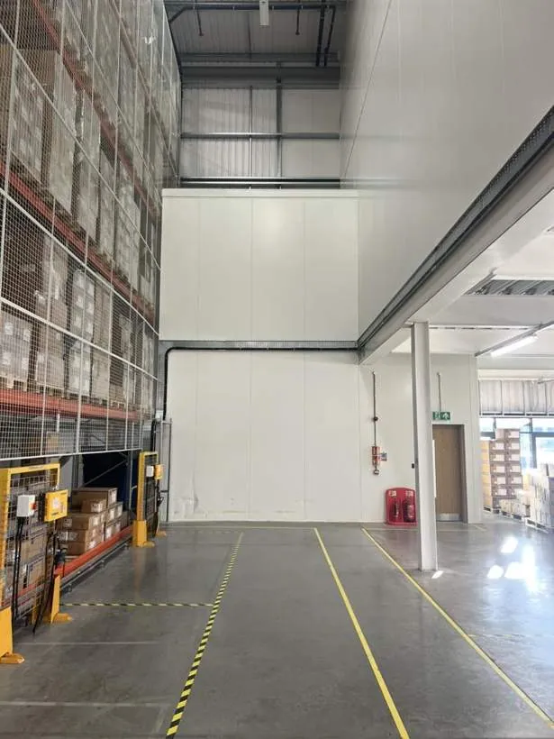 High-level galvanised cable tray carrying charger supplies across a warehouse wall above the racking, Bicester