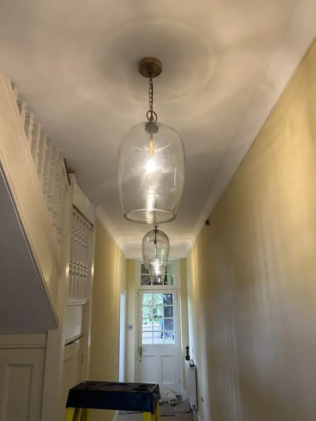 Two glass lantern pendants lighting a long period hallway towards a garden door