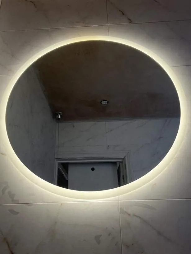 Large round LED backlit mirror glowing on a marble-effect bathroom wall, Brackley