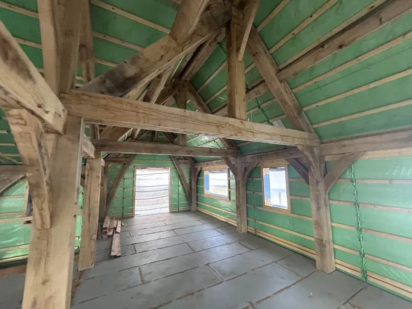 Oak frame self-build shell with exposed timber trusses and breather membrane before any electrical work, village near Bicester