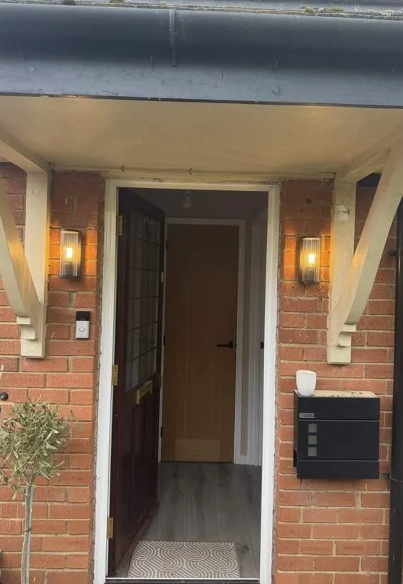 Pair of outdoor wall lanterns lit either side of a front door under a timber porch canopy, Bicester