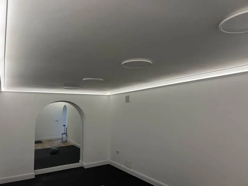 Basement home gym with warm LED cove lighting around the ceiling edge, flush round ceiling lights and an arched opening, Chinnor