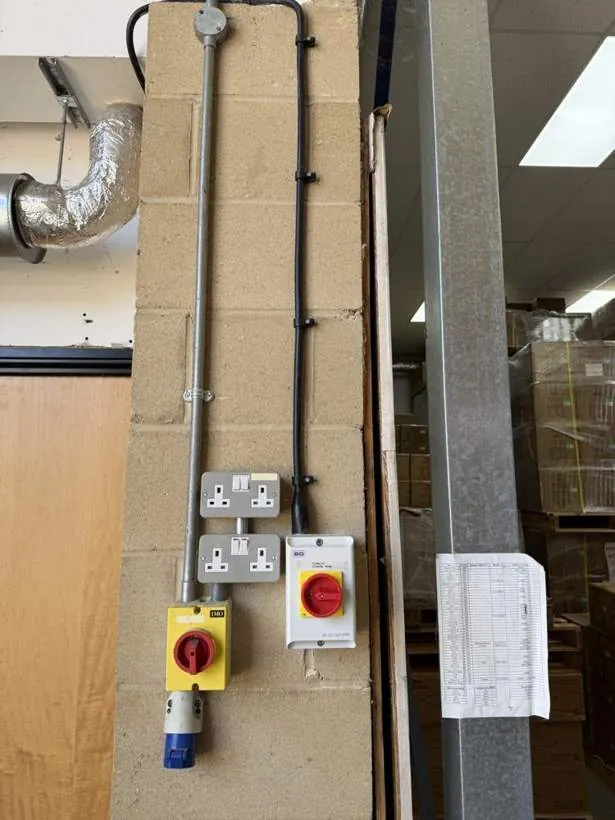 Steel conduit with new double sockets, a rotary isolator and an industrial socket on a blockwork wall in a commercial unit in Bicester