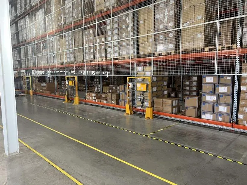 Row of relocated forklift chargers in protective frames along a warehouse racking aisle, Bicester