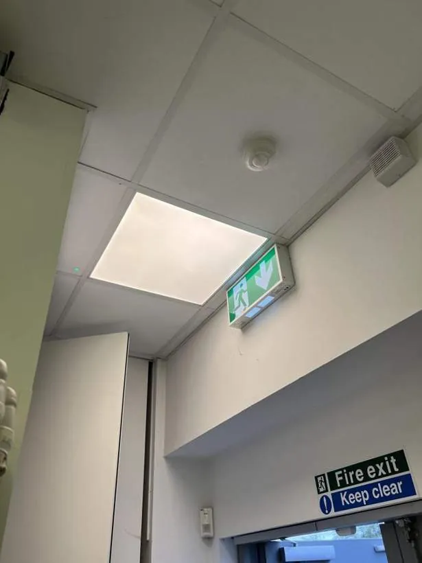 Retail unit ceiling with a new 600 by 600 emergency LED panel and illuminated exit sign, Bicester Village