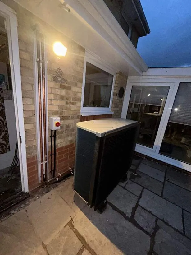 Heat pump outdoor unit beside a rotary isolator on an external brick wall, Buckinghamshire