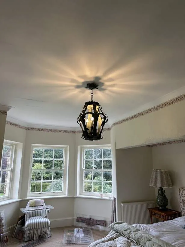 Black metal lantern pendant light casting a pattern across the ceiling of a bay-windowed bedroom