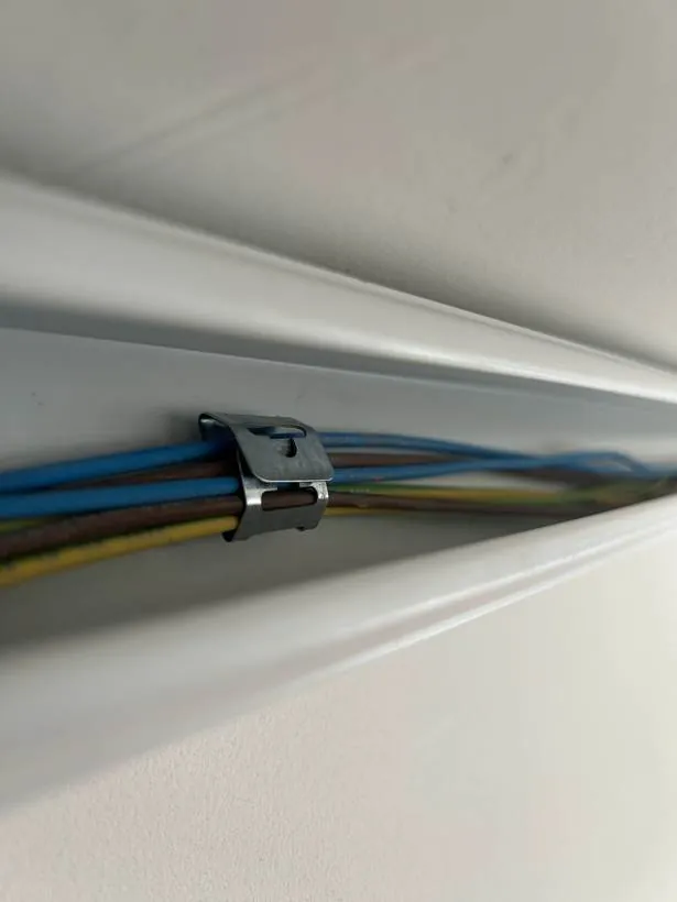 Close-up of cables in trunking held by a metal fire-rated clip, as required by BS 7671, during a commercial fit-out in Banbury