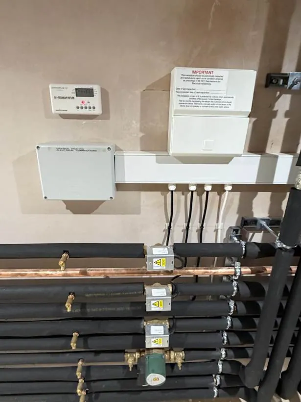 Neatly wired heating zone valves, wiring centre, programmer and consumer unit above insulated pipework in a plant room, Bloxham