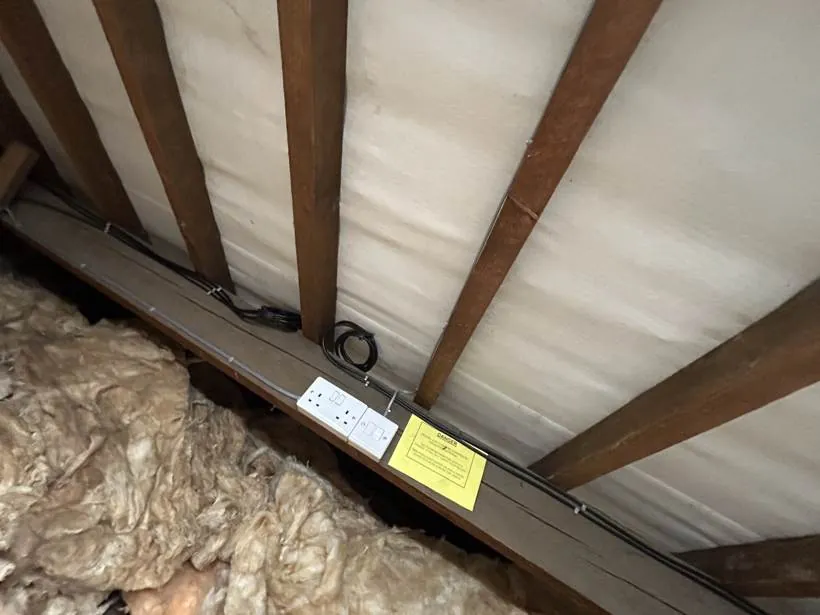 Double socket and light switch on a loft timber with neatly clipped cable runs, part of a full rewire in Oxford