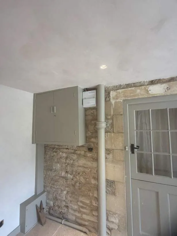 New grey consumer unit enclosure on a wall beside exposed Cotswold stone and existing pipework, Charlbury