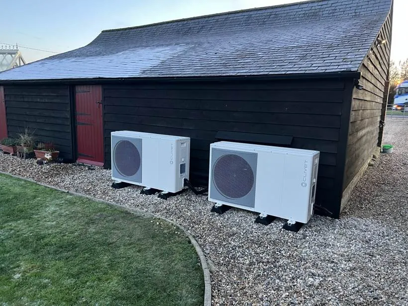 Two air source heat pump outdoor units side by side beside a timber outbuilding, Buckinghamshire